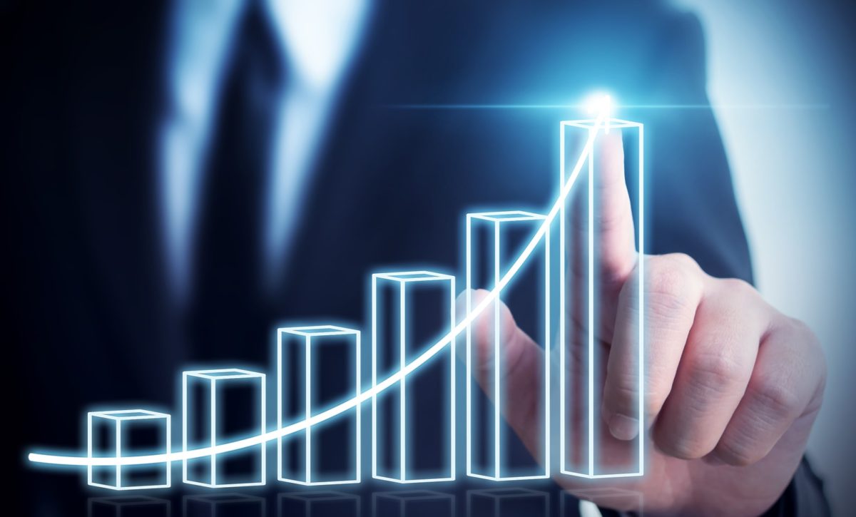 Businessman in dark suit pointing to the highest point of a 3D bar graph